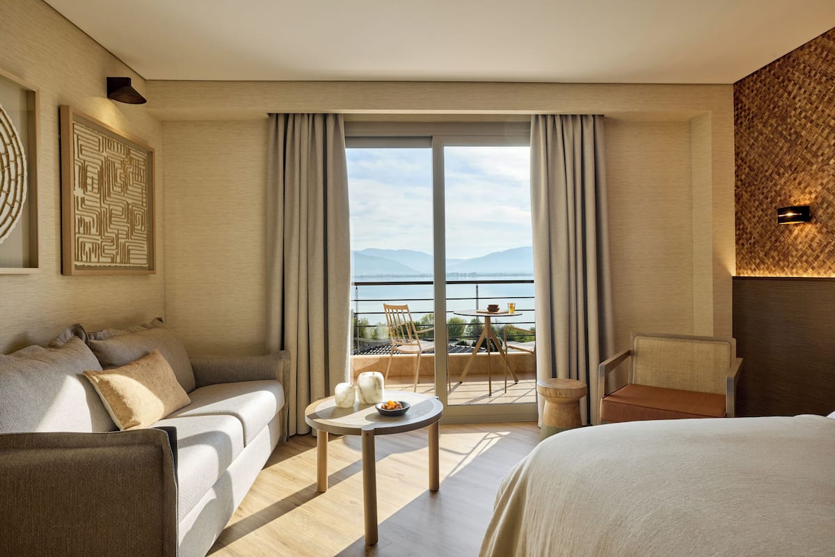 A hotel room with a balcony, a sofa, a bed, a small table with fruits, and a view of the sea.