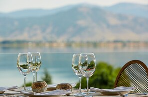 Una mesa dispuesta con copas de vino y un plato, con vistas a un lago y montañas al fondo.
