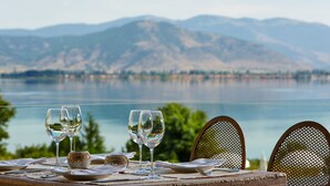 A table set with wine glasses and a rustic tablecloth, overlooking a lake with mountains in the background. - Limneon Resort & Spa (Kastoria)