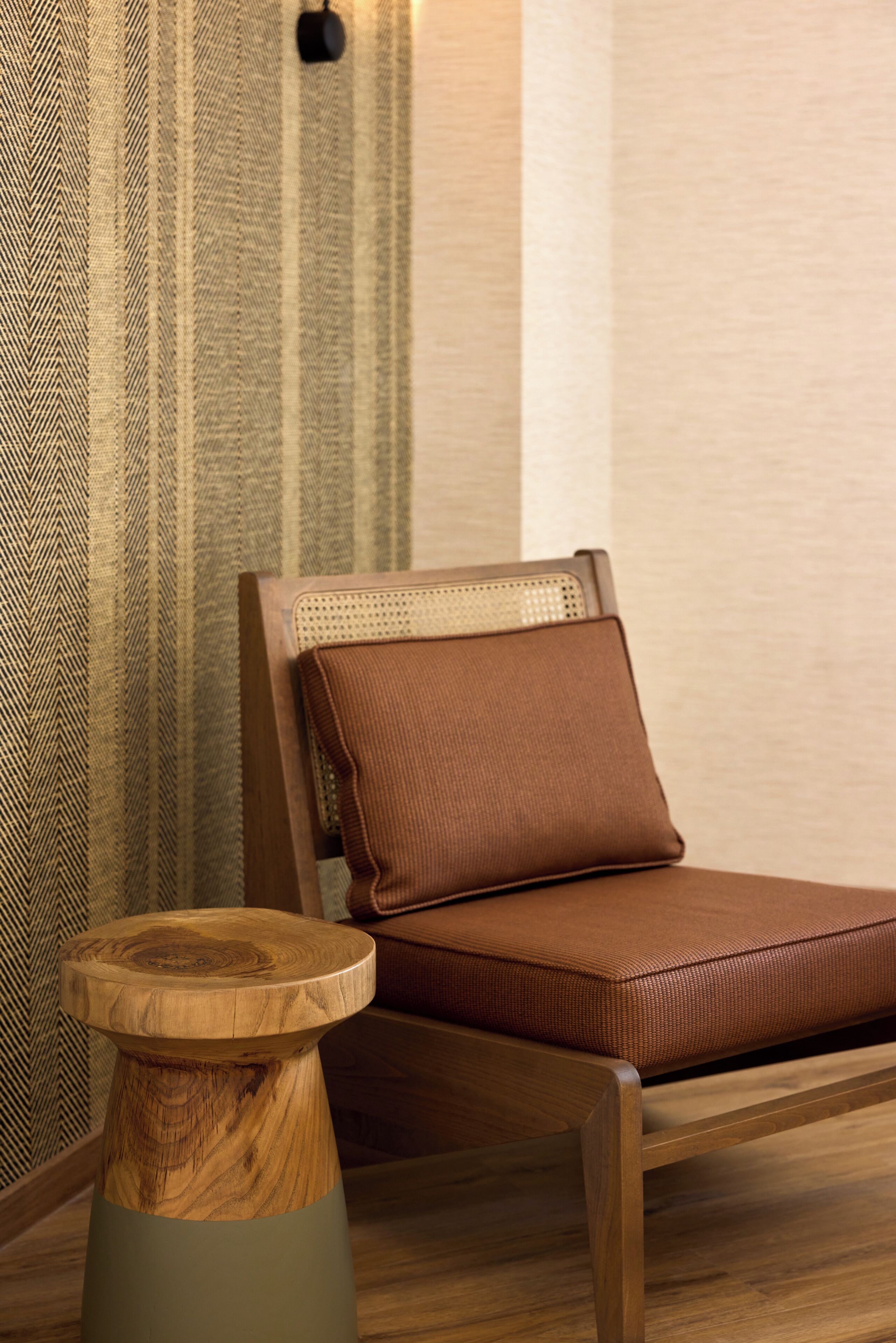 Une chaise en bois avec un coussin, un tabouret en bois et un mur orné de motifs.