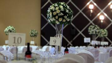 Una mesa con un florero de vidrio con flores blancas, carteles con números y botellas de vino.
