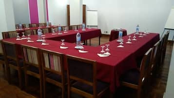 Un salón de conferencias con mesas largas, sillas, botellas de agua y copas de vino.