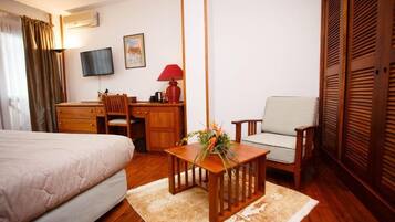 Habitación de hotel con cama, escritorio, silla, televisor y ventana con cortinas.