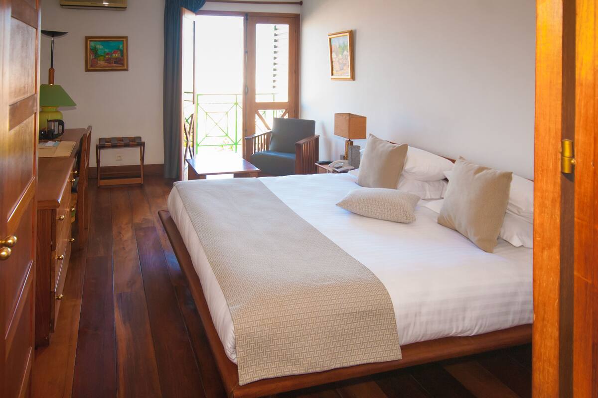 A hotel room with a large bed, wooden furniture, a desk with a lamp, and a chair.
