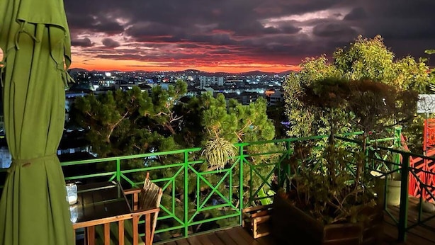 A balcony with a view of a cityscape at sunset, featuring a railing and potted plants. - Palissandre Hotel & Spa (Antananarivo)