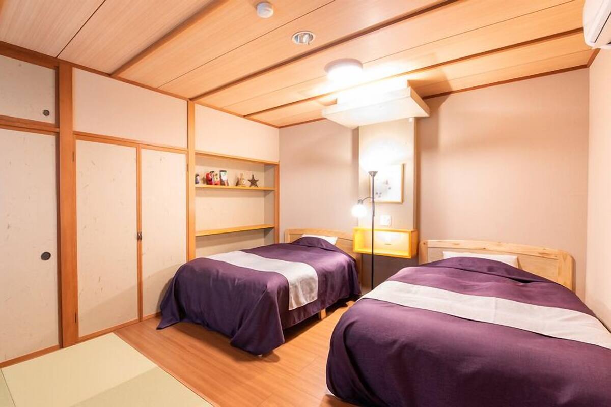 Une chambre avec deux lits, un plancher en bois, une étagère avec divers objets et un miroir.