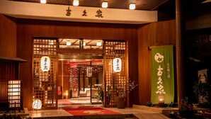 Egy hagyományos japán bejárat, melynek része a fa ajtó, a piros szőnyeg és a japán írásjegyekkel díszített zöld zászló.