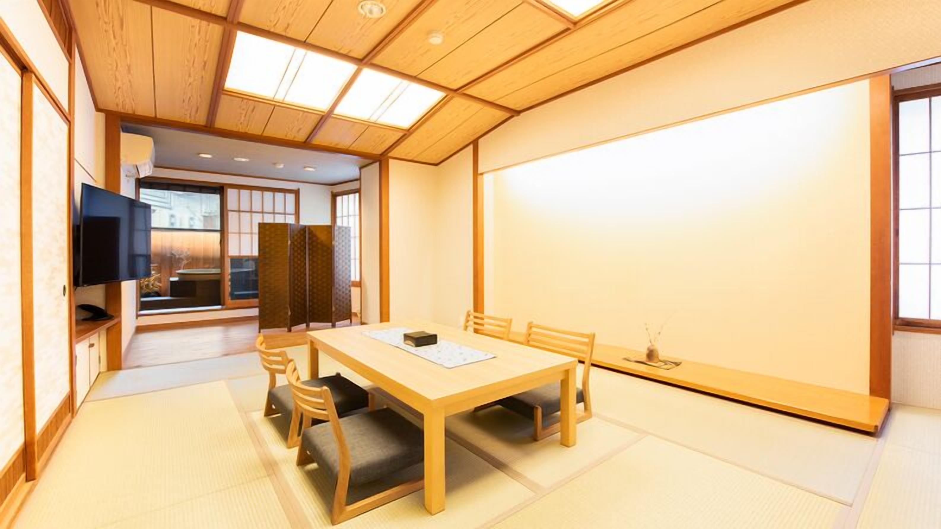 A traditional Japanese-style room with tatami flooring, a low wooden table, and a television mounted on the wall.
