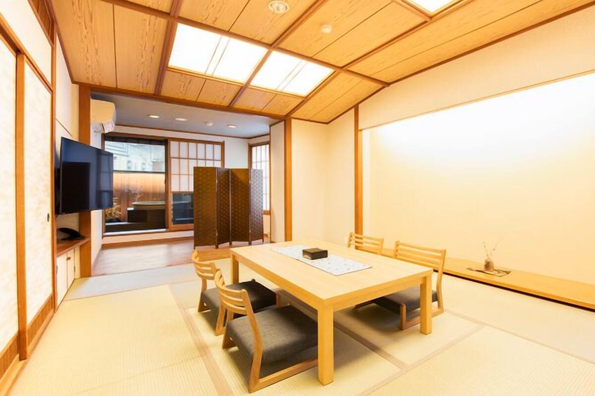 Une pièce de style japonais traditionnel, avec un sol recouvert de tatamis, une petite table en bois et un téléviseur fixé au mur.