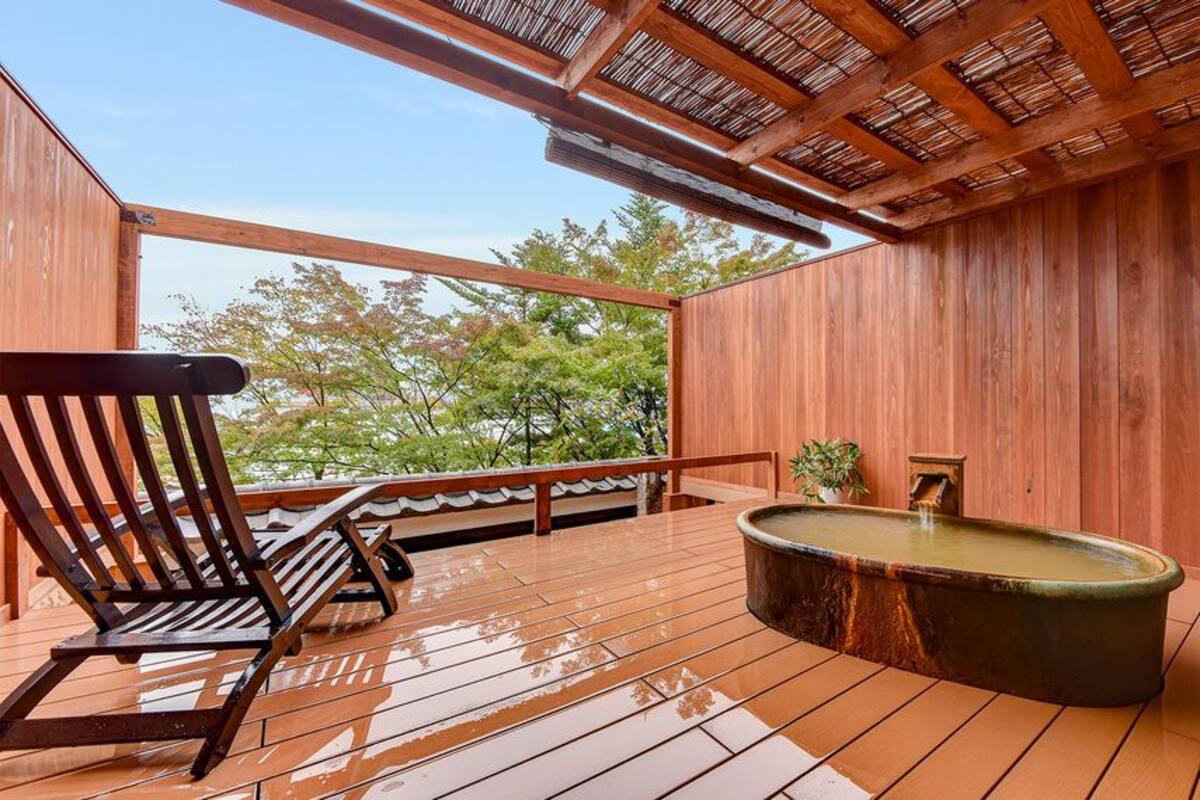 Une terrasse en bois avec un jacuzzi, une chaise en bois et une rambarde.