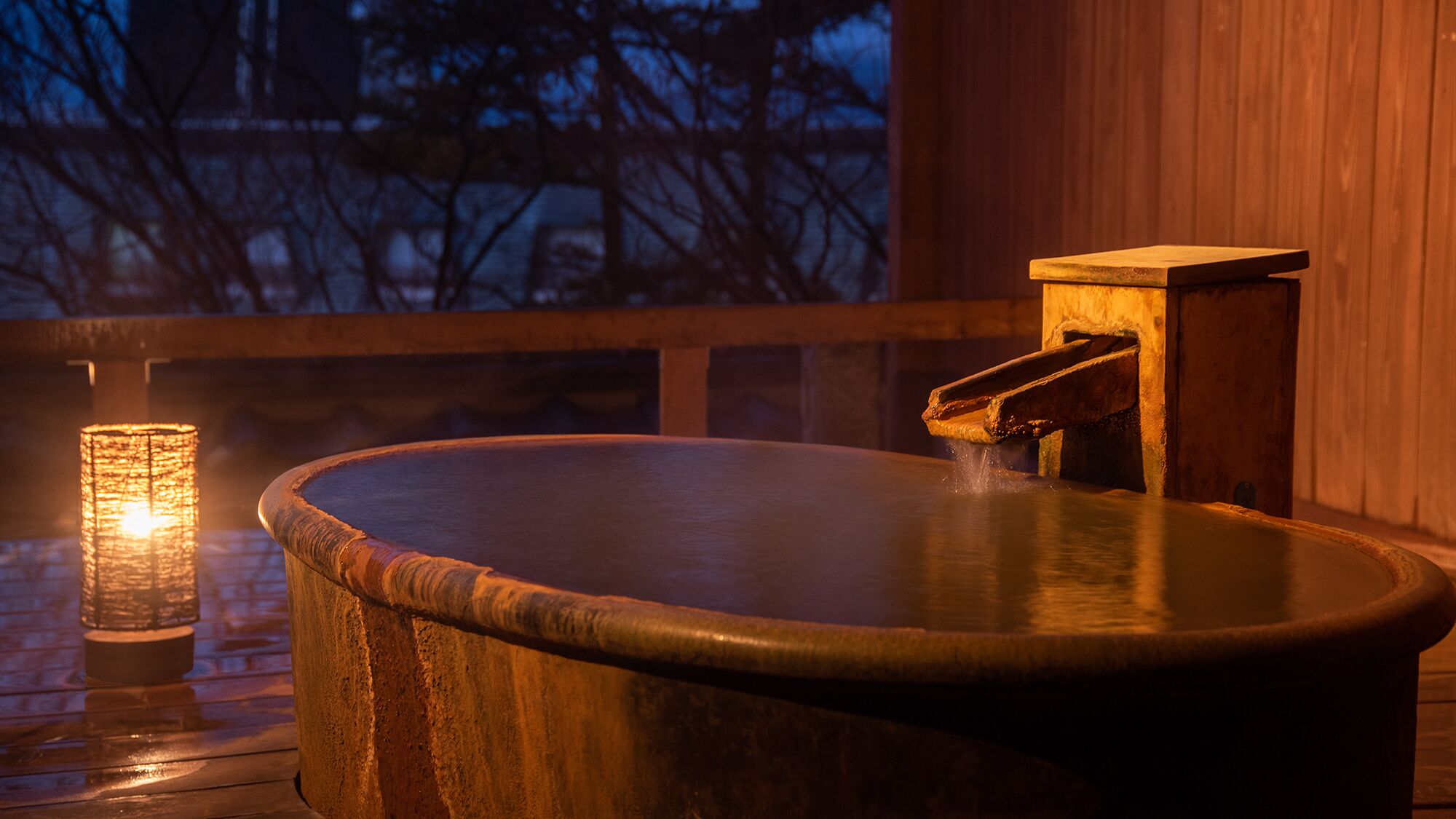 A wooden hot tub with a faucet, a candle, and a wooden deck.