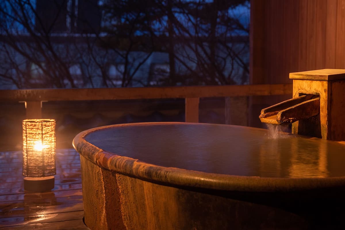 Un bain à remous en bois, doté d’un robinet, d’une bougie et d’une terrasse en bois.