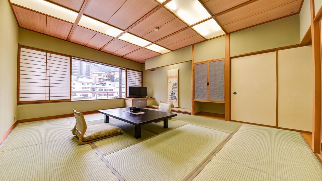 A traditional Japanese room with tatami flooring, a television, a desk, and sliding doors.