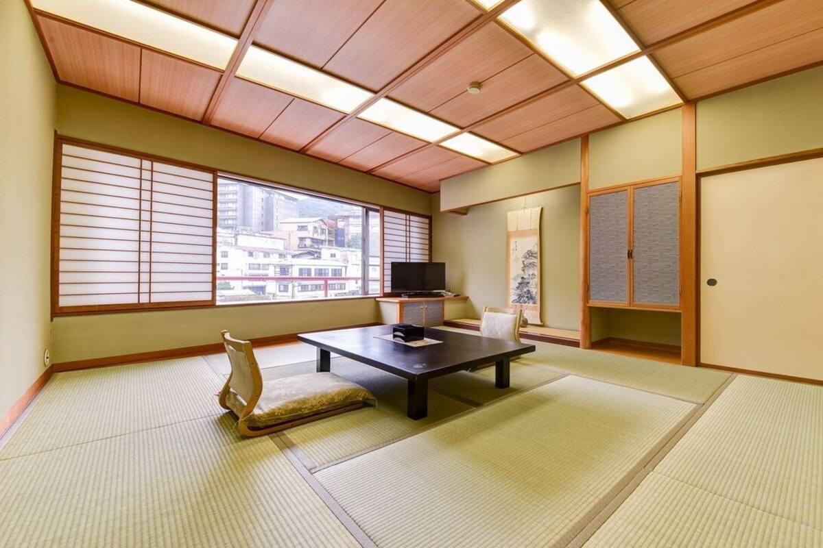 Une pièce de style japonais traditionnel, avec un sol recouvert de tatamis, une télévision, un bureau et des portes coulissantes.