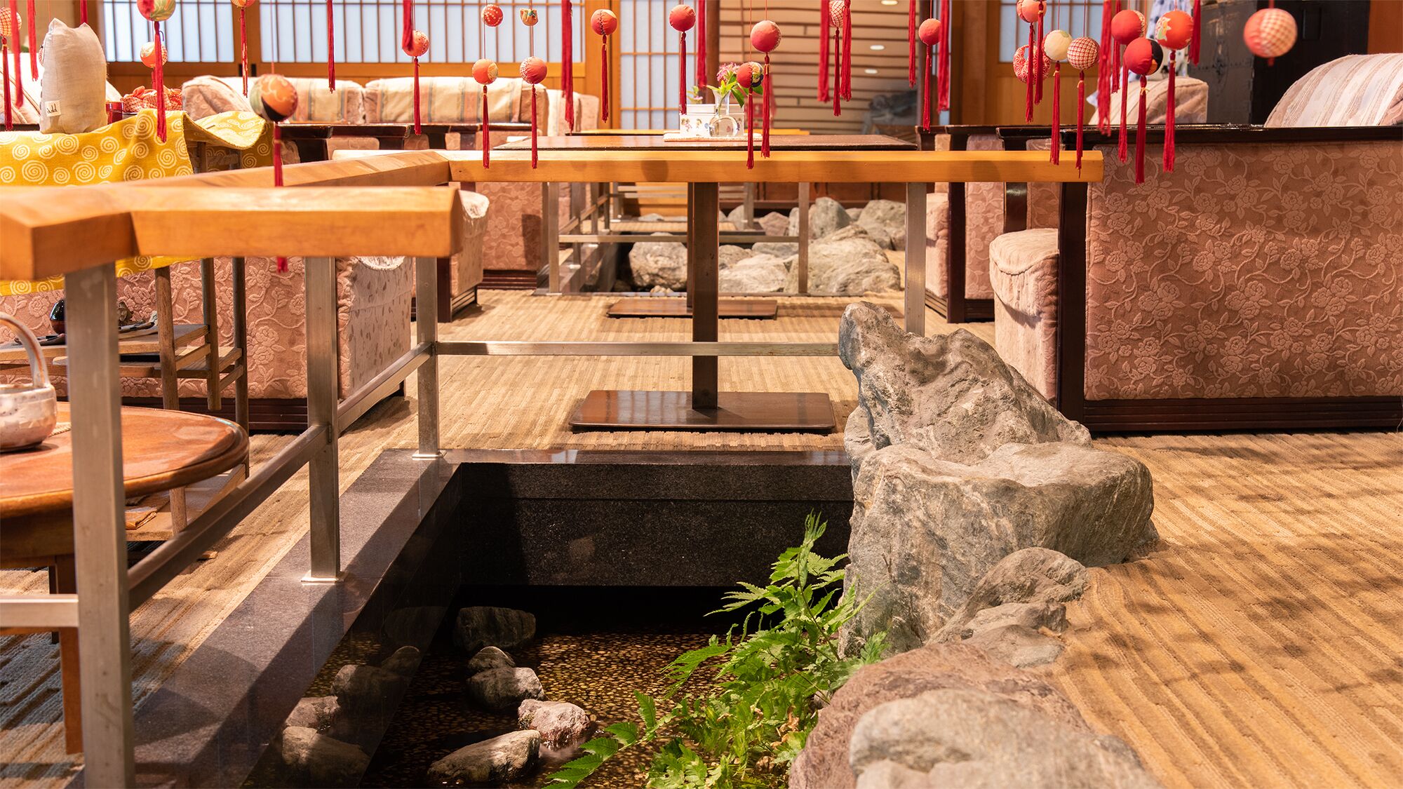 Un interior tradicional japonés con esteras de tatami, un jardín de rocas y adornos rojos colgantes.
