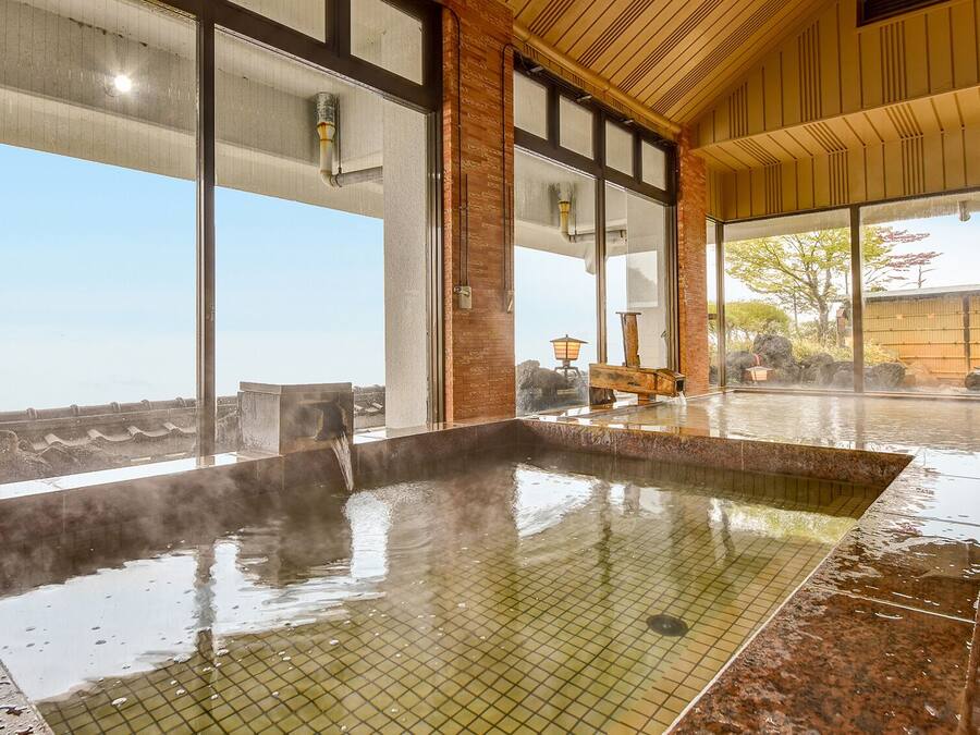A hot spring bath with a tiled floor, large windows, and a wooden ceiling.