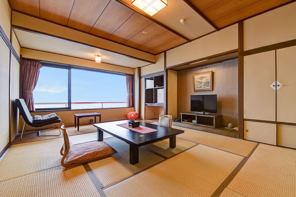 Une pièce de style japonais traditionnel, avec un sol recouvert de tatamis, une télévision, une porte coulissante et une vue sur le ciel.