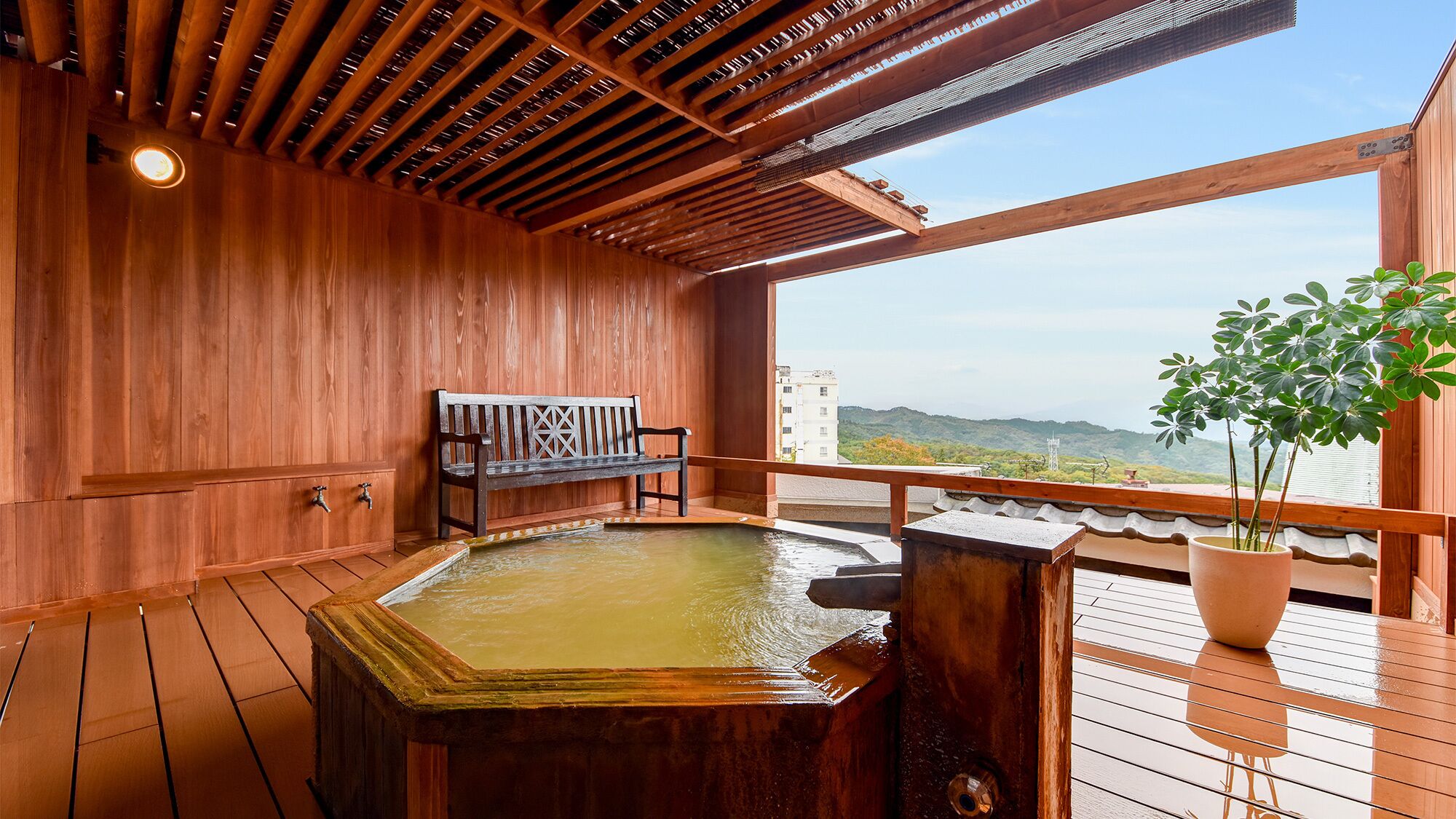 A wooden deck with a hot tub, a bench, and a potted plant.
