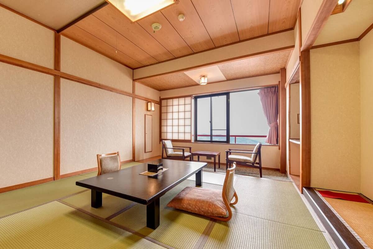 Une pièce de style japonais traditionnel, avec un sol recouvert de tatamis, une table basse, des chaises et une porte coulissante.