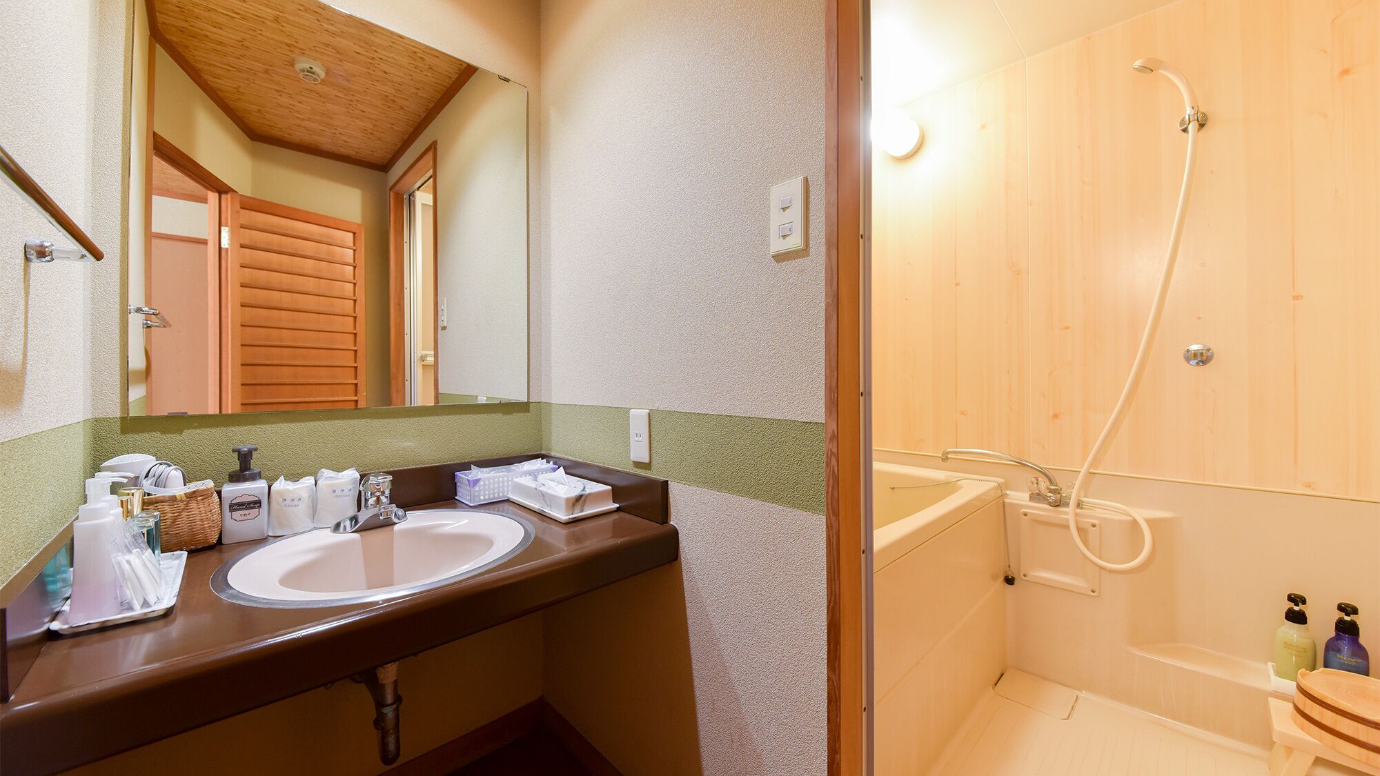 A bathroom with a wooden shower, a sink with toiletries, and a mirror.