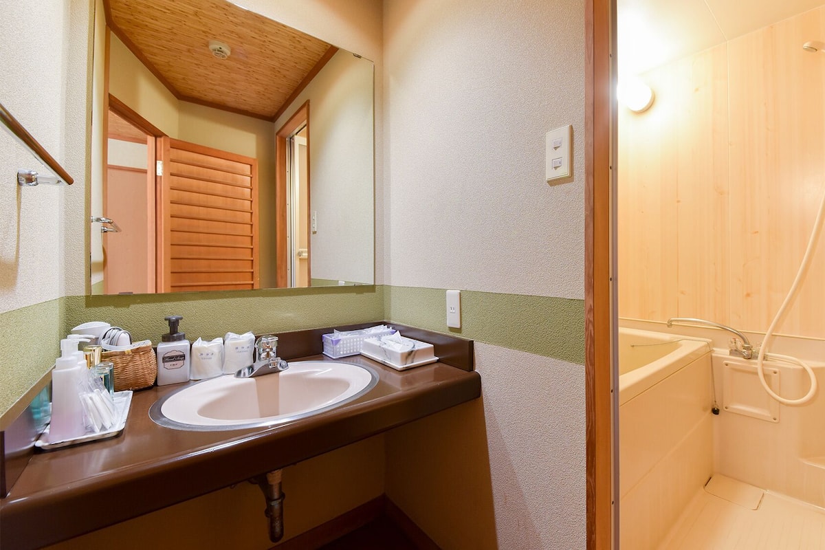 Une salle de bain avec une douche en bois, un lavabo avec des articles de toilette et un miroir.