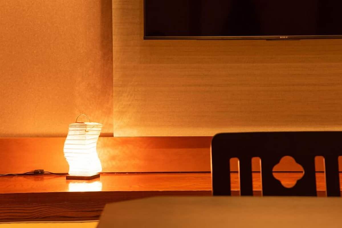 Une chambre d’hôtel avec un téléviseur fixé au mur, une chaise en bois et une table avec une lampe.
