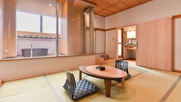 Une pièce de style japonais traditionnel, avec un sol recouvert de tatamis, une table basse et une porte coulissante donnant sur un espace cuisine.