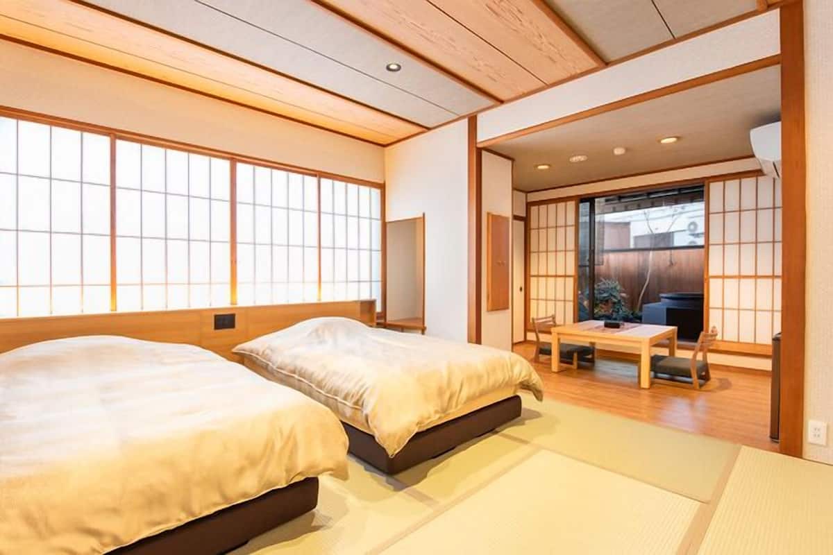 Une pièce de style japonais traditionnel, avec un sol recouvert de tatamis, deux lits, une porte coulissante donnant sur un balcon et un plafond bas en bois.