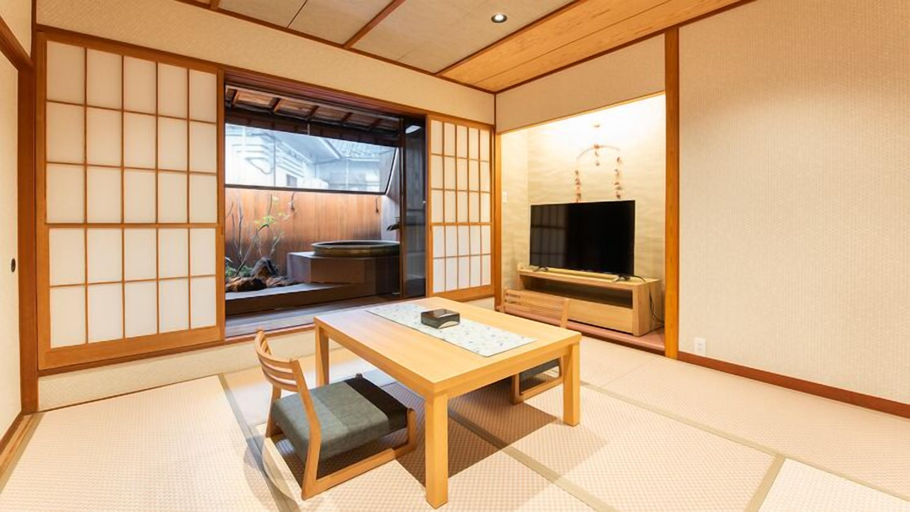 A traditional Japanese room with tatami flooring, a low table with a cushion, a television, and sliding doors.