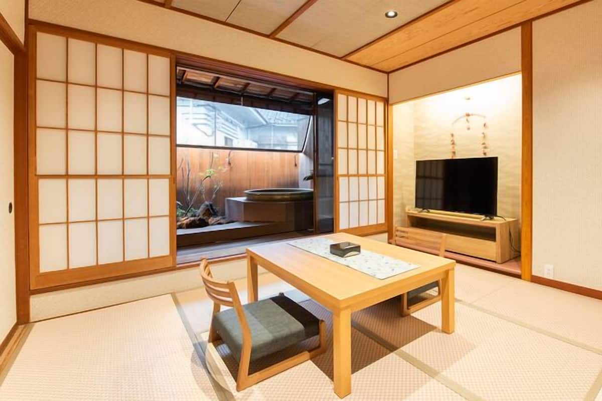 Une pièce de style japonais traditionnel, avec un sol recouvert de tatamis, une petite table basse avec un coussin, un téléviseur et des portes coulissantes.