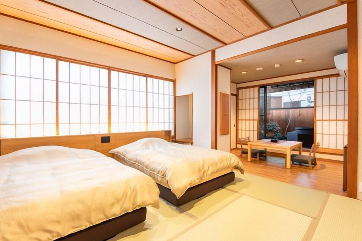 A traditional Japanese-style room with tatami flooring, two beds, a sliding door leading to a balcony, and a low wooden ceiling.