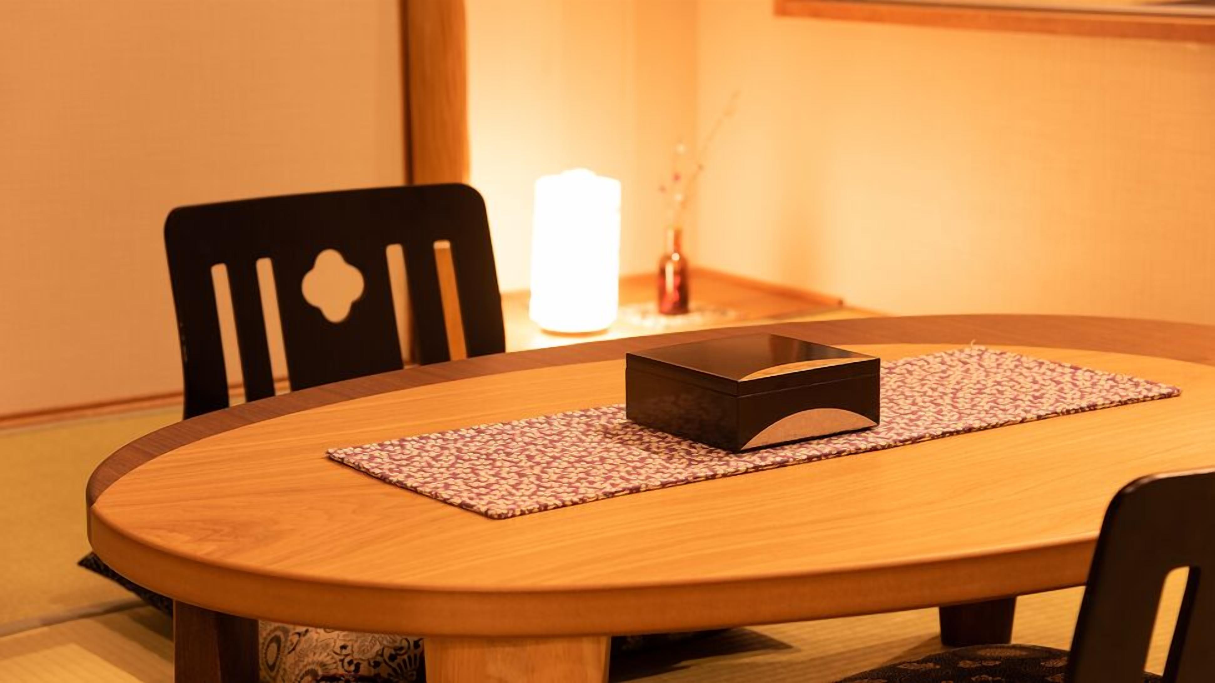 A round wooden table with a dark rectangular object on a patterned placemat, surrounded by black chairs.