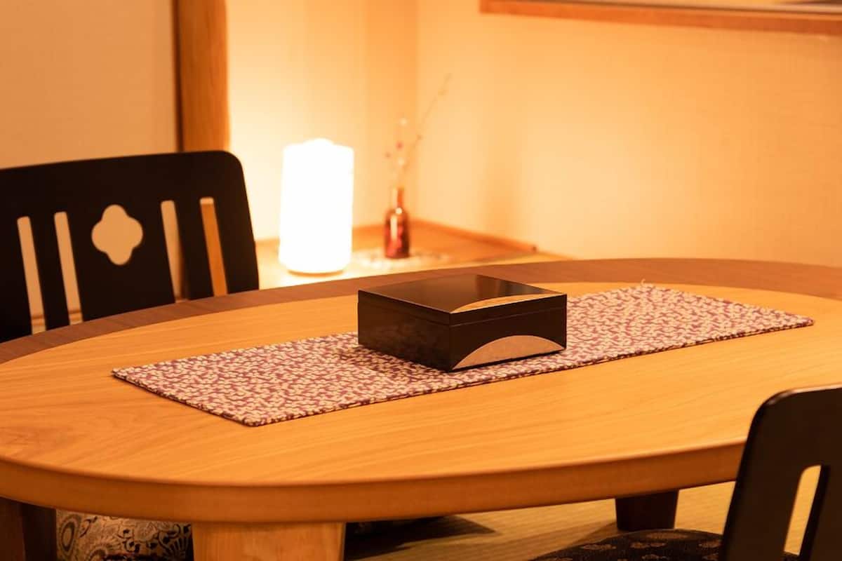 Une table ronde en bois, sur laquelle repose un objet rectangulaire foncé, le tout posé sur un set de table à motifs, et entourée de chaises noires.