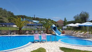 A swimming pool with a slide, lounge chairs, and umbrellas. - Pension Nychterida (Corfu)