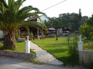 Un chemin menant à un bâtiment doté d’un espace extérieur abrité, entouré de verdure et de palmiers.