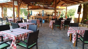 An outdoor café with checkered tablecloths, wicker chairs, and a stone floor. - Pension Nychterida (Corfu)