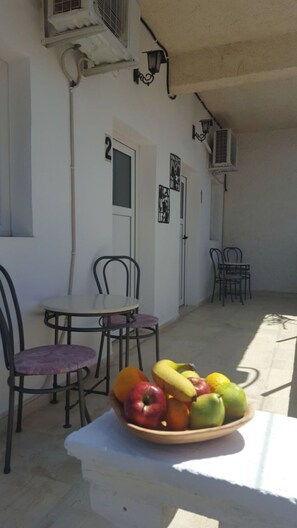 Zona exterior amb seients, taula i cadires, un bol de fruita i aparells d'aire condicionat a la paret.