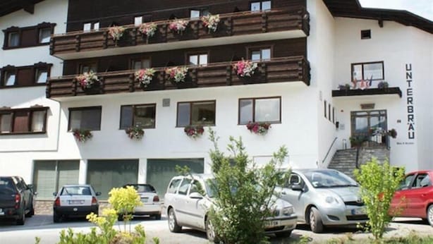 Un edificio de varios pisos con balcones decorados con flores, una escalera que lleva a la entrada y coches estacionados en primer plano.