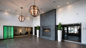 Eine geräumige Lobby mit Kamin, großen Topfpflanzen und moderner Pendelleuchten.