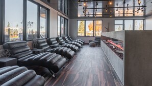 Ein moderner Spa-Raum mit mehreren Massagesesseln, einem Kamin und großen Fenstern mit Blick ins Freie.