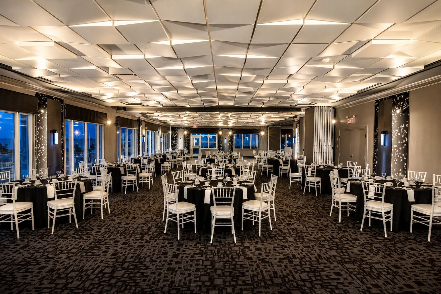 A large conference room with multiple tables and chairs, a patterned carpet, and a ceiling with recessed lighting.