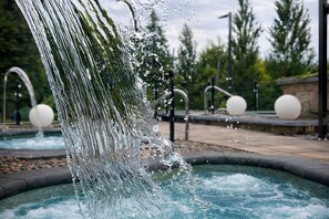Una fuente con un gran chorro de agua y estructuras esféricas en un área ajardinada.