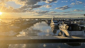Ein Yachthafen mit Booten, die an einer Holzsteg liegen und den Sonnenuntergang spiegeln.