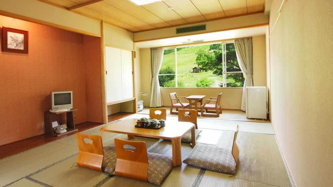Une pièce de style japonais traditionnel, avec un sol recouvert de tatamis, une petite table basse avec des coussins et un téléviseur posé sur un meuble.