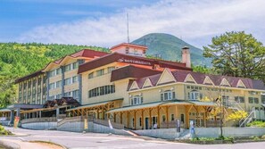 Un hôtel à plusieurs étages, avec un toit rouge, un espace extérieur couvert et une montagne en arrière-plan.