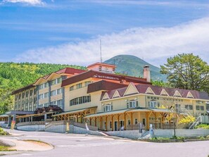 Un hotel de varios pisos con techo rojo, un espacio al aire libre cubierto y montañas al fondo.