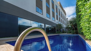 Un hotel moderno con piscina, ventanas amplias y un jardín bien cuidado.