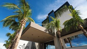 Una entrada de hotel moderna con palmeras, cielo despejado y un gran letrero que dice "Catuña Hotel".