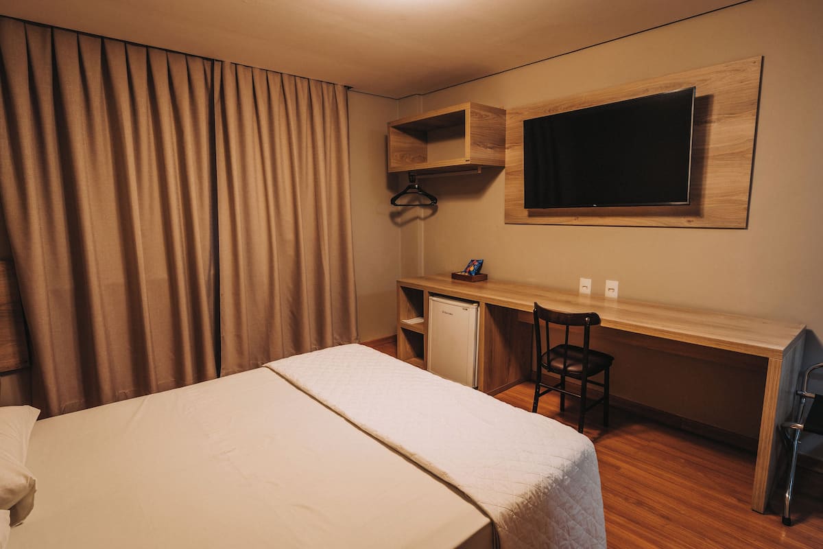 A hotel room with a bed, a desk with a chair, a television, and a small refrigerator.