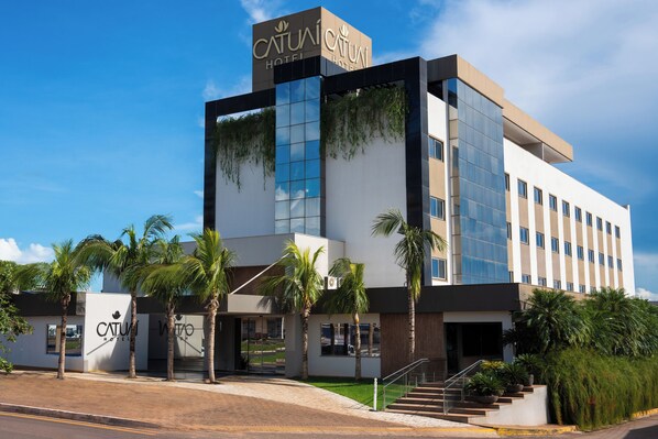 A modern hotel with a glass facade, palm trees, and a clear sky. - Catuai Hotel (Cacoal)